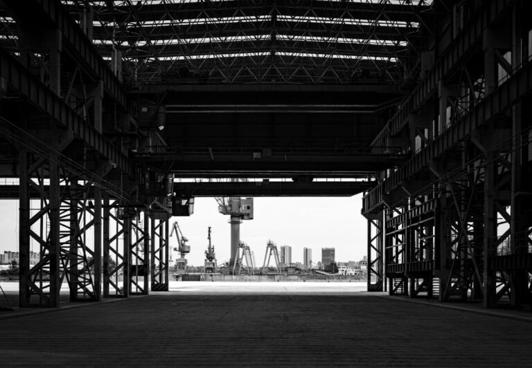 Black and white view from industrial building towards port cranes.