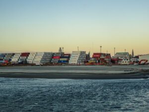 Shipping containers stacked at a port with calm water.