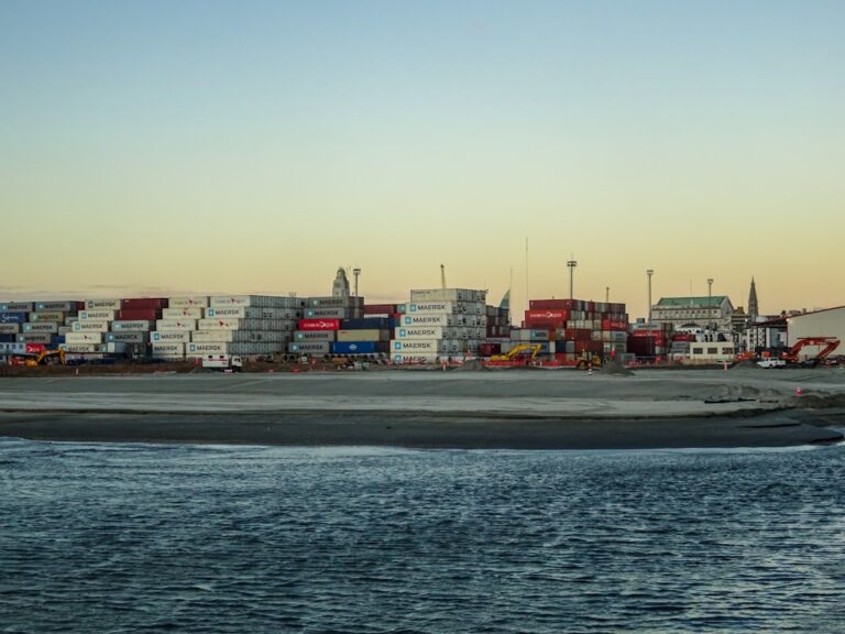 Shipping containers stacked at a port with calm water.