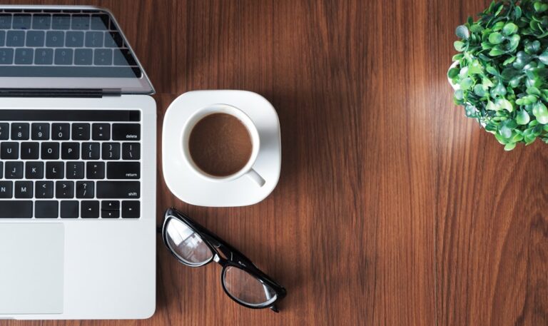 Laptop, coffee, and plant on a wooden desk.